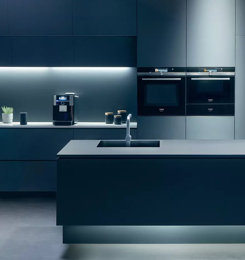 Moderne dunkelgraue Designküche von Siemens mit Kochinsel, flächenbündiger Spüle und hochwertig integrierten Siemens Geräten, indirekt beleuchtet.