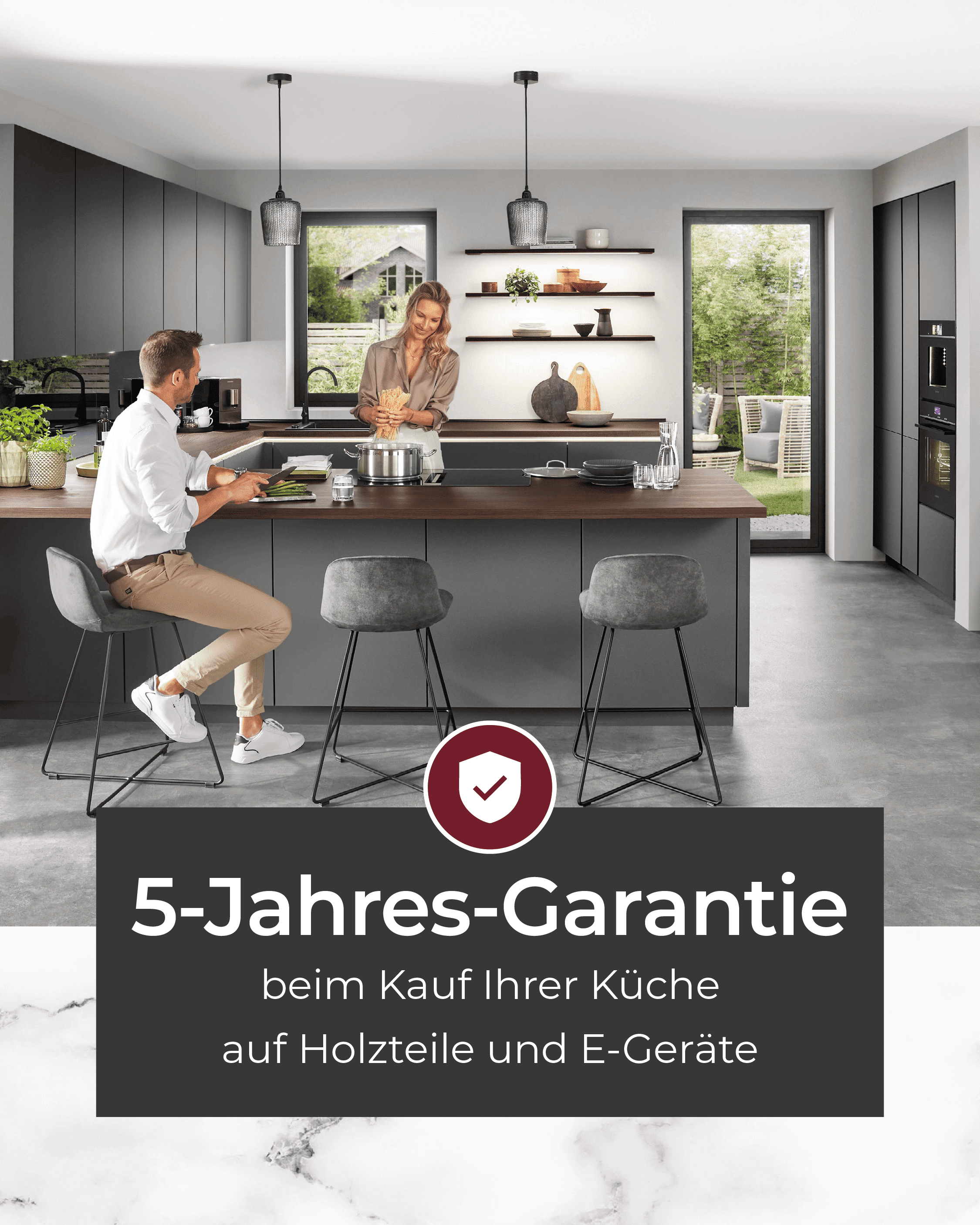 Designküche in dunklem Grau mit Kochinsel und Paar beim Kochen – Hinweis auf 5-Jahres-Garantie beim Küchenkauf auf Holzteile und Elektrogeräte